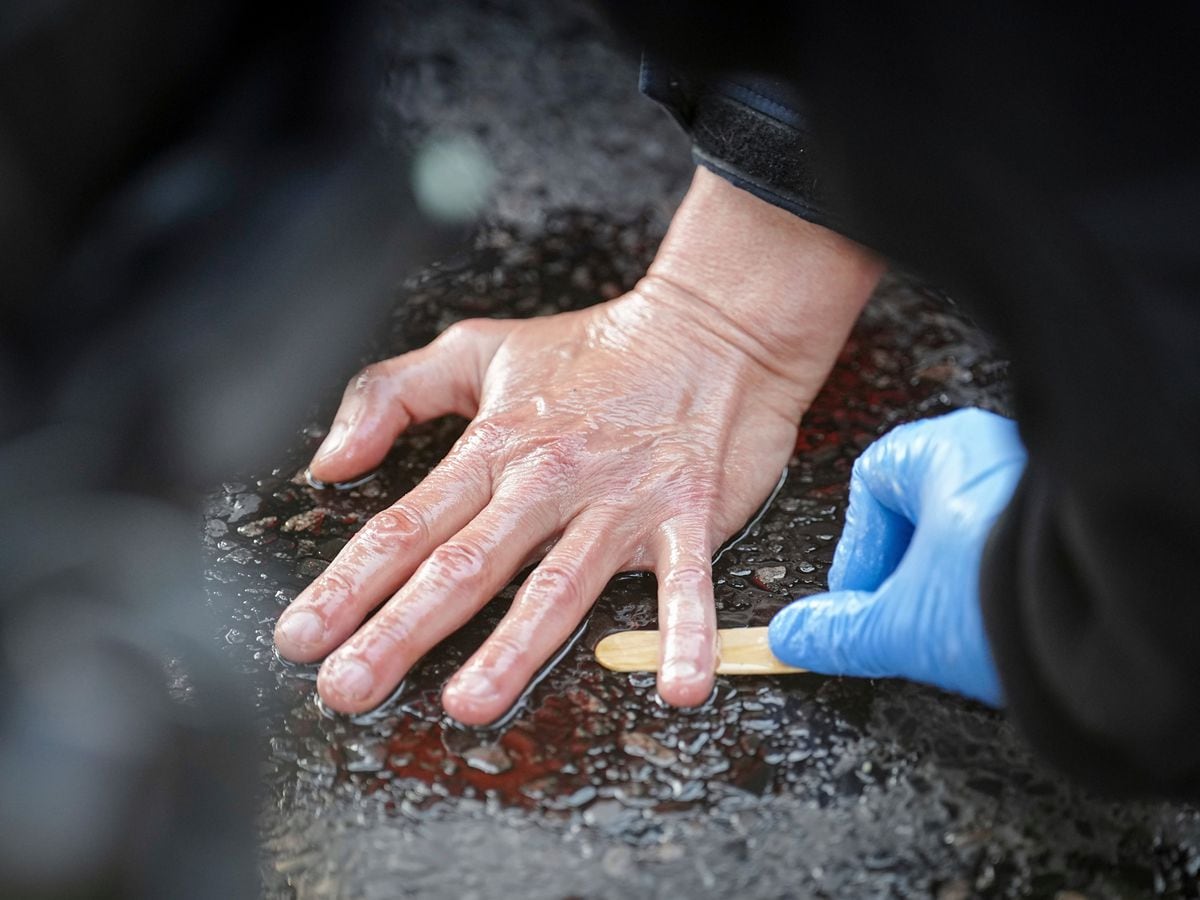 A police officer unglues the hand of a climate activist from the road in front of the Victory Column, Berlin