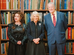 The Queen stands in front of packed bookshelves at The London Library with Helena Bonham Carter and Sir Stephen Fry