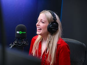 A smiling Lauren Laverne wearing headphones in front of a BBC 6 Music microphone