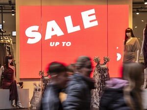 Shoppers walking past a sale sign in a shop window