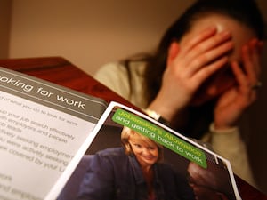 A woman holds her head in her hands with Job Seeker's leaflets in front of her