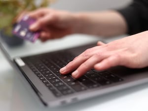 Woman typing on a laptop, holding her bank card in her spare hand