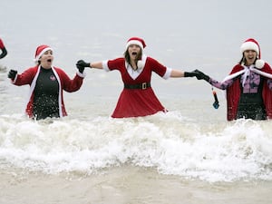 Three women in Christmas outfits stand waist-deep in the waves