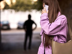 A woman looking over her shoulder while on a mobile phone and looking back at a figure in silhouette