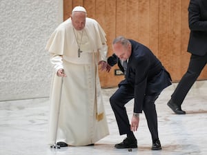 Pope Francis’ aide leans down to pick up the the handle of the Pope’s walking stick