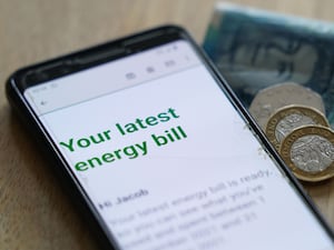 An energy bill is displayed on a smartphone next to bank notes and coins