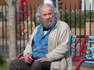 Paul Bradley as Nigel Bates sitting on a bench in a scene from EastEnders