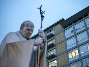 A statue of the late Pope John Paul against a backdrop of the Gemelli hospital