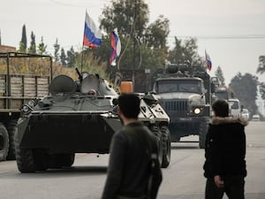 Syrian fighters watch Russian armoured vehicles driving near the Hmeimim air base