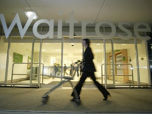 A person pushing a trolley past a Waitrose store