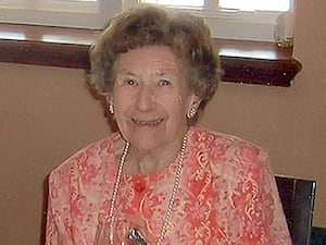 Una Crown, smiling, and wearing a pink blouse, pearl necklace and earrings