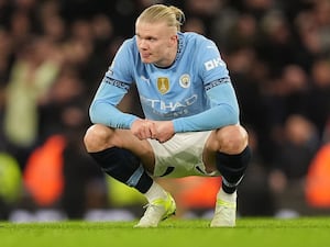 Manchester City striker Erling Haaland squats with his elbows on his thighs