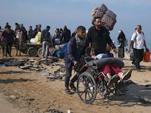 A displaced Palestinian pushes an elderly woman in a wheelchair on a road to return to their homes in the northern Gaza Strip