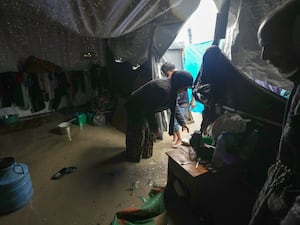 A woman tries to clean her flooded tent after heavy overnight rain at a refugee camp in in Deir al-Balah, Gaza Strip