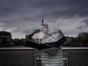 A person takes shelter under an umbrella as they cross a bridge