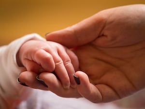 An adult hand holding a baby's hand