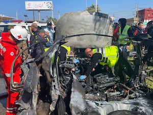 Civil Defence workers inspect the remains of a burned car that was hit by an Israeli drone strike