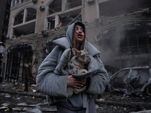 A woman warms her dog in front of a destroyed burning car after a recent Russian attack in Kyiv, Ukraine