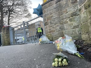 Flowers outside All Saints Catholic High School as a police officer stands at the gates