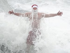 Waves crash over a sea swimmer dressed in a Santa hat and beard