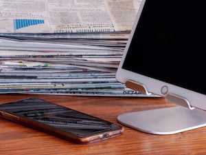 A mobile phone and tablet near a stack of newspapers