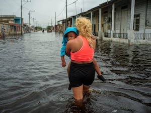 A woman carries a child as she wades through a street flooded in the passing of Hurricane Helene