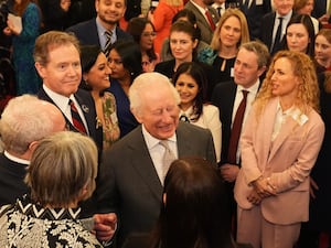 The King laughing with his eyes shut surrounded by people during a reception at Buckingham Palace for newly elected Members of Parliament and members of the House of Lords