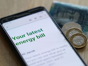 An online energy bill on a mobile phone next to coins and cash