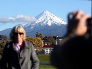 A man takes a picture of his wife with Mount Taranaki in the background