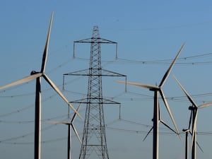 Wind turbines stand next to an electricity pylon