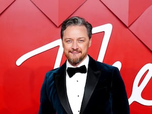 James McAvoy dressed in a suit and bow tie, standing in front of a red wall