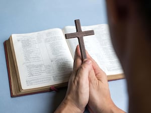 Person holding small cross in prayer over a Bible