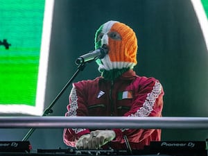 A member of Kneecap on stage wearing a woollen hat in the Irish colours