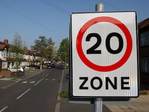 A 20mph speed limit sign on a road with houses on it