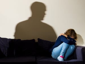 A shadow of a man with a clenched fist as a woman cowers on a sofa