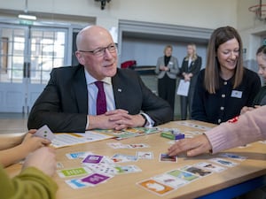 John Swinney smiles as he sits at a table in a classroom