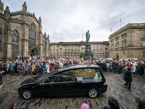 Crowd of people look on as a hearse passes