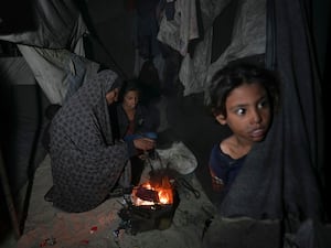 A family displaced from the northern Gaza Strip sit round a fire in their tent at a camp in Deir al-Balah