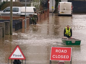 A flood warden pushes a boat in floodwater behind signs with 'flood' and 'road closed' on them