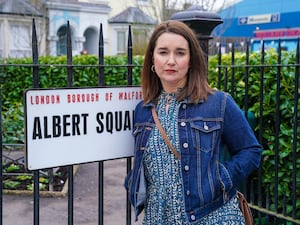 Alice Haig as Vicki Fowler standing next to the Albert Square sign