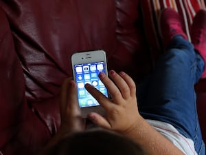 A young child lies on a couch while playing on a smartphone