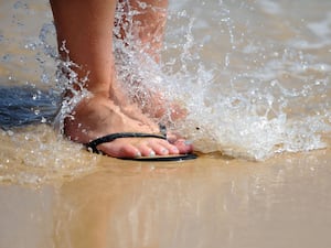 Waves lap over feet in flip flops on a beach