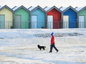 A man walks his dog near the beach huts on Blyth beach, Northumberland, on the north east coast