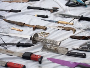 Various knives and knuckle-dusters laid out on a white cloth