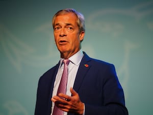 Nigel Farage in a blue suit and pink tie in front of a light blue background