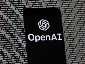 The OpenAI logo on a mobile phone in front of a computer screen with random binary data