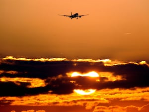 Plane flies in to Heathrow Airport above a sunrise through clouds