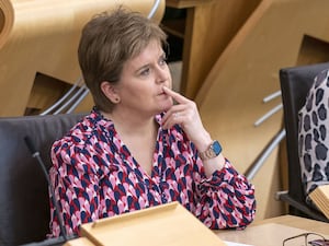 Nicola Sturgeon seated in Holyrood, with one hand resting on her face