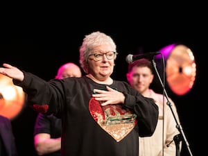 Janey Godley gesturing with a hand while speaking on a stage