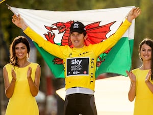 Geraint Thomas lifts the Wales flag while wearing the yellow jersey after winning the Tour de France